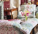 Upholstered chair and chaise lounge with colorful floral patterned fabric in a room with a fireplace and side table.