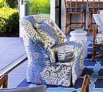 Upholstered chair with blue and white patterned fabric on a blue outdoor patio with seating.
