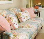 Couch with colorful patchwork fabric and pink pillows, in a room with a small table and window.