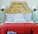 Bedroom with yellow floral headboard, blue pillows, red blanket.