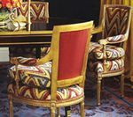 Ornate dining chairs with patterned cushions, gold frames, red backs, near a table.