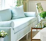 Light blue sofa with white accents in a well-lit room; side table with glass top and decorative flowers.