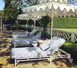 Lounge chairs with blue patterned cushions under white umbrellas with scalloped edges; outdoor setting.