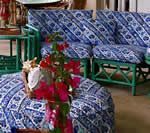Blue patterned cushions on green rattan furniture; red flowers in vase.