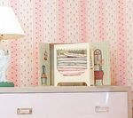 Pink dresser with open box containing folded linens, wallpaper background with pink dots.