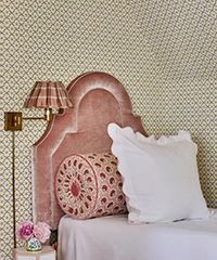Pink velvet headboard with white and patterned pillows, plaid lamp, and patterned wallpaper.