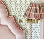 Pink velvet headboard, plaid lampshade, brass sconce against patterned wallpaper.