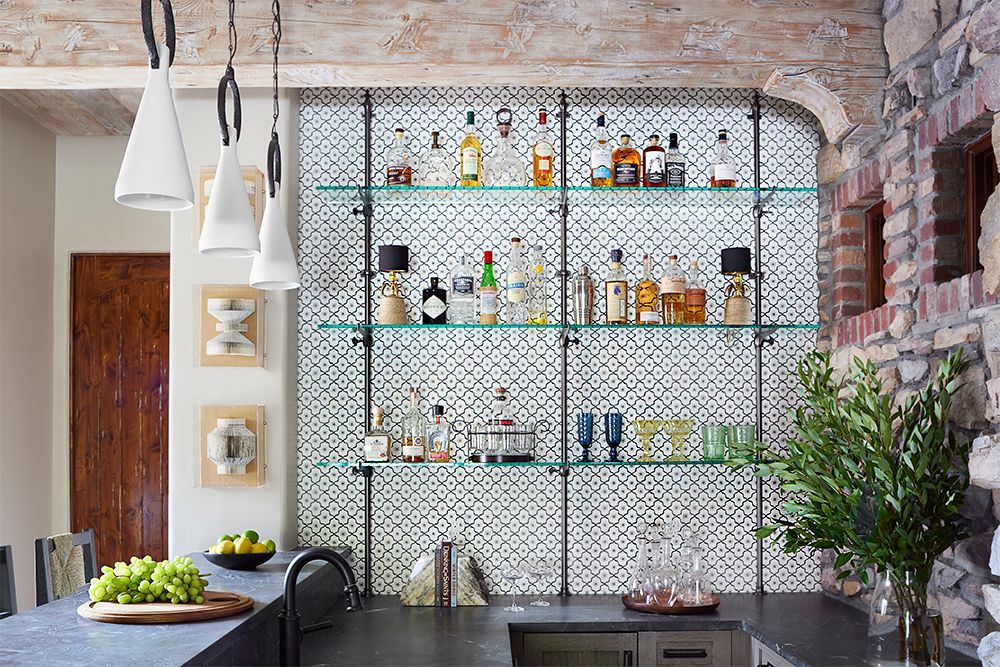 Bar with liquor bottles on glass shelves against a patterned backdrop, next to a stone wall.