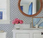 Bathroom with blue patterned wallpaper, white vanity, round wooden mirror, and pink flowers.