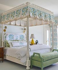 Four-poster bed with floral canopy, white bedding, and green bench in a bedroom.