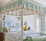 Bedroom with a four-poster bed and light blue floral accents. A yellow lamp sits on the bedside table.