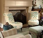 Two floral armchairs facing a fireplace, with a small ottoman in the foreground.