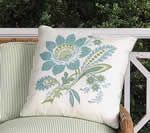 Square white pillow with blue floral design on striped chair outdoors.