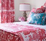 Bedroom with red and white patterned bedding and curtains, teal accent pillows, and a bedside lamp.