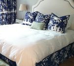 Bedroom with white bedding, blue patterned pillows and skirt, and blue patterned curtains.