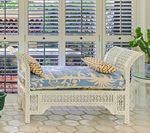 White wicker daybed with blue patterned cushion, window shutters, and tiled floor.