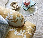 Close-up of patterned pillows in gold and blue on a sofa with a tray of snacks and a drink.