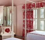 Bedroom with white canopy bed, red floral curtains, and white chair with red pillow.