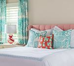 Bedroom with pink headboard, white bedding, turquoise patterned curtains and pillows, and a red lamp.