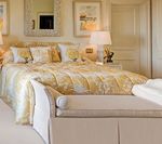 Bedroom with yellow and cream bedding, matching bench, bedside lamps, and decorative mirrors.