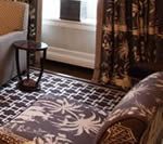 A room with a patterned rug, chaise lounge, side table, curtains, and radiator.