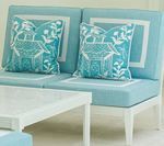 Blue outdoor seating with white trim and pillows with house design. White table in foreground.