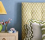 Bedroom with blue wall, patterned headboard, nightstand, lamp, and decorative pillows.