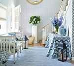 Elegant blue and white foyer with floral arrangements, two white benches, patterned rug, and a staircase.