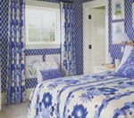 Blue and white bedroom with patterned wallpaper, curtains, and floral bedspread.