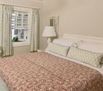 Bedroom with a bed covered in a red pattern quilt, window with striped curtains, and a lamp on the nightstand.