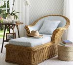 Wicker chaise lounge with blue patterned cushion, hat, and pillow. Beside it is a small table and woven stool.
