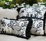 Two black and white patterned pillows with ruffled edges rest on a beige couch, outdoor setting.