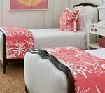 Two twin beds with white sheets and coral floral bed runners and pillows in a bedroom.