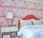 Bedroom with pink toile wallpaper, coral headboard, white bedding, and a pink lamp.