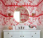Red and white floral wallpapered bathroom with white vanity, gold mirror, and sconces.