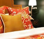 Bed with orange floral and yellow pillows, white sheets, and a gold lamp.