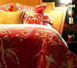 Red floral comforter and pillows on a bed with a gold headboard; bedside table visible.