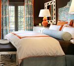 Bedroom with a bed, bench, curtains, lamp, and mirror; features orange, blue, and brown accents.