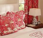 Red and white bedroom with decorative pillows, curtains, lamp, and bedside table.