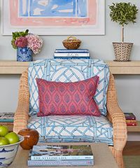 Wicker armchair with blue patterned cushion and pink pillow, by a small table with books.
