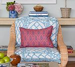 Wicker chair with blue and white patterned cushion, pink pillow, and shelf with decor.
