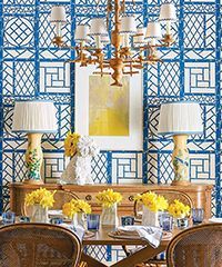 Dining room with blue trellis wallpaper, chandelier, table set for meal, and yellow floral arrangements.