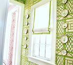Window in a room with green trellis wallpaper and decorative plates. White trim, Roman shade.