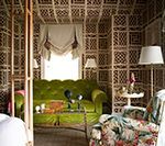 Room with green sofa, floral chair, lattice walls, lamps, and a window with valance.