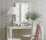 A white console table with a lamp, mirror, decor, and a palm frond in front of a bamboo-patterned wall.