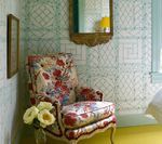 Floral armchair in room with patterned wallpaper, gold mirror, yellow floor, flowers.