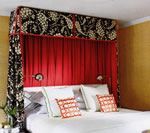 Bedroom with bed and red curtains. Black and white floral patterned canopy frame over the bed.