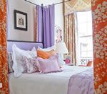 Bedroom with a lavender headboard and curtains, orange floral patterned curtains, and a framed picture.