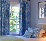 Bedroom with blue patterned curtains, pillows, and light blue walls.