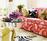 Brightly decorated living room with a red patterned sofa, coffee table, and zebra rug.